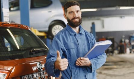 Mechanic in coveralls with a clipboard giving thumbs up in a garage