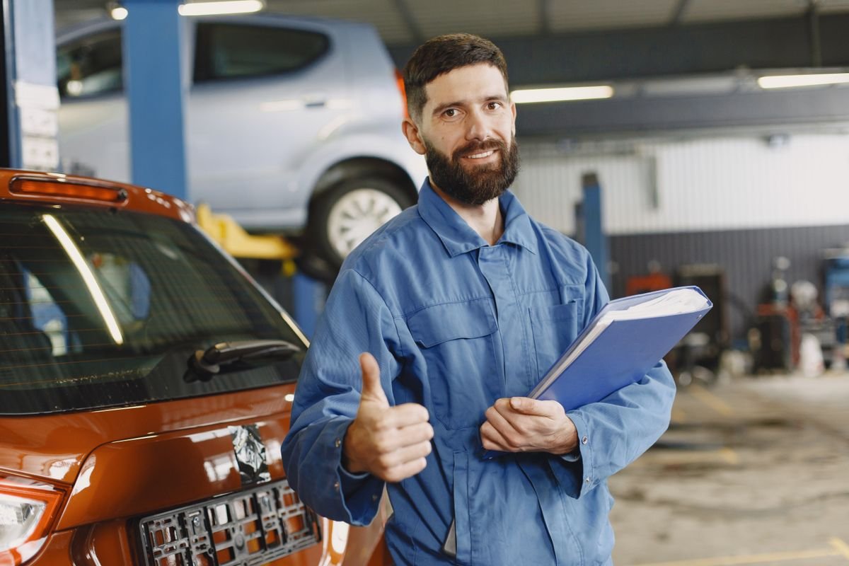 Mechanic in coveralls with a clipboard giving thumbs up in a garage